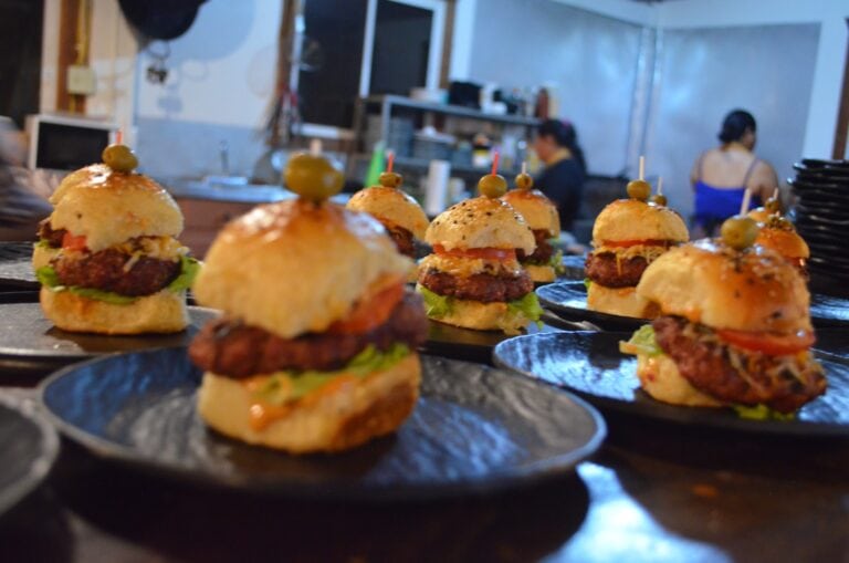 Delicious sliders with beef patties, lettuce, and toppings on small black plates.