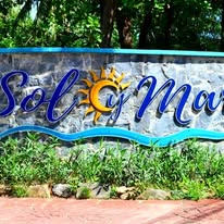 A colorful sign for Sol y Mar, a business located in Roatan, Honduras, featuring blue and yellow lettering with a sun graphic and lush greenery in the background.
