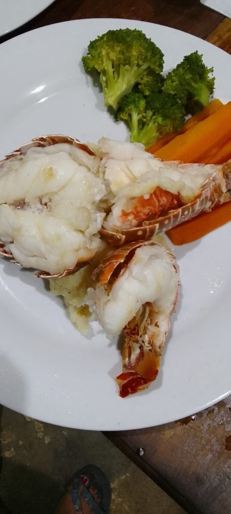 Cooked lobster served with mashed potatoes and steamed broccoli and carrots on a white plate in Roatan, Honduras.
