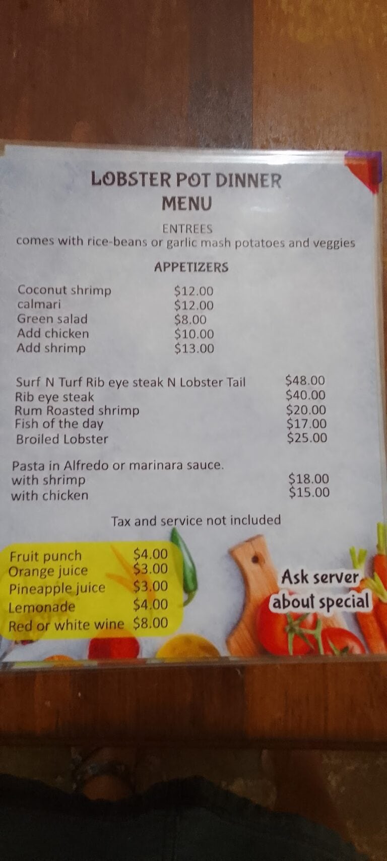 A Lobster Pot dinner menu displayed on a table in Roatan, Honduras, featuring seafood dishes, appetizers, fruit drinks, and options for rice, beans, and garlic mash potatoes.