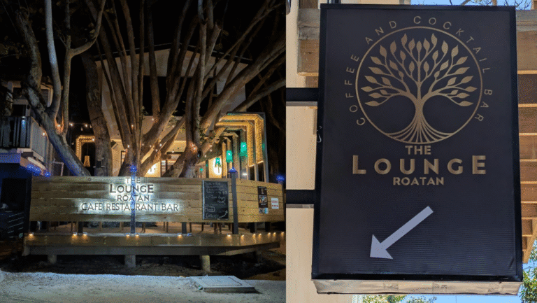 The image shows the entrance to The Lounge Roatan, a cafe and restaurant bar in Roatan, Honduras, with illuminated signage and a large wooden deck surrounded by trees and decorative lighting.