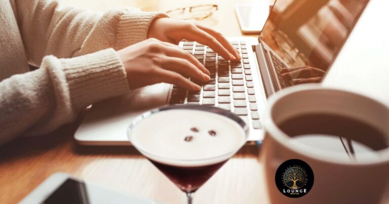A person working on a laptop with a cup of coffee and a cocktail featuring coffee beans on top, set on a wooden table at a cozy cafe in Roatan, Honduras.