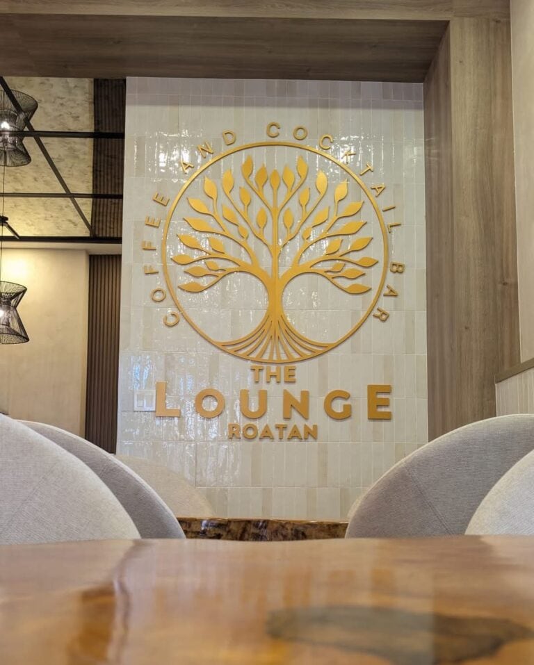 A wall featuring a gold logo of a tree with the words "The Lounge Roatan" and "OFFER AND COCTAIL BAR" displayed inside a circular design in a stylish indoor setting in Roatan, Honduras.
