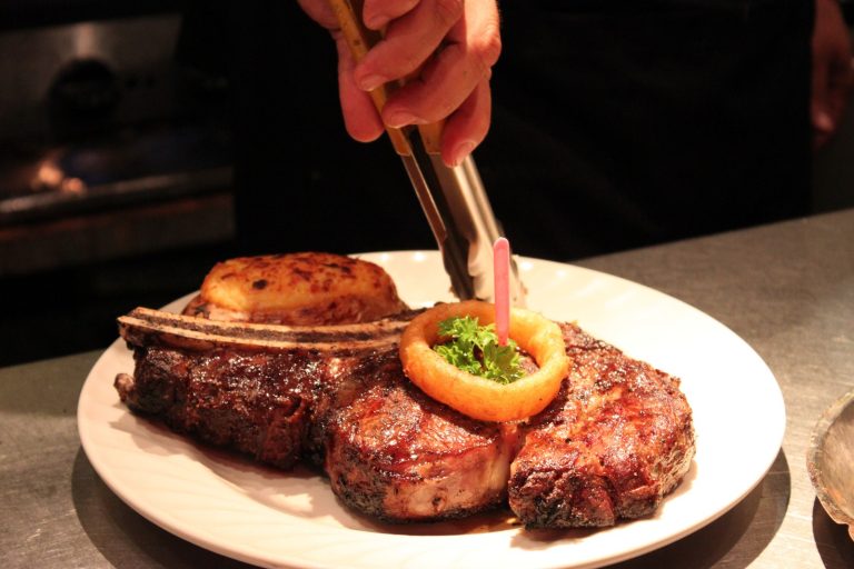 A grilled steak served with a baked potato, onion ring, and garnished with a sprig of parsley on a white plate at a restaurant in Roatan, Honduras.