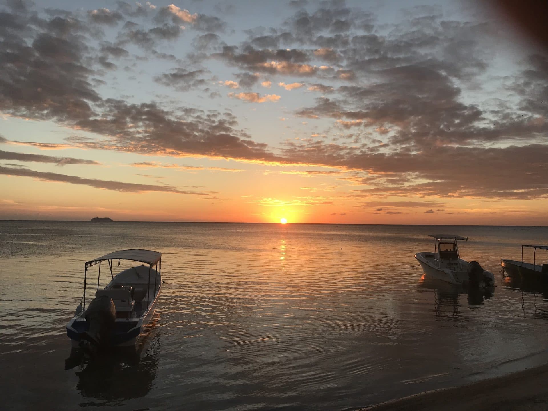 A scenic sunset over the ocean in Roatan, Honduras, with boats docked along the calm water and a small island visible in the distance.