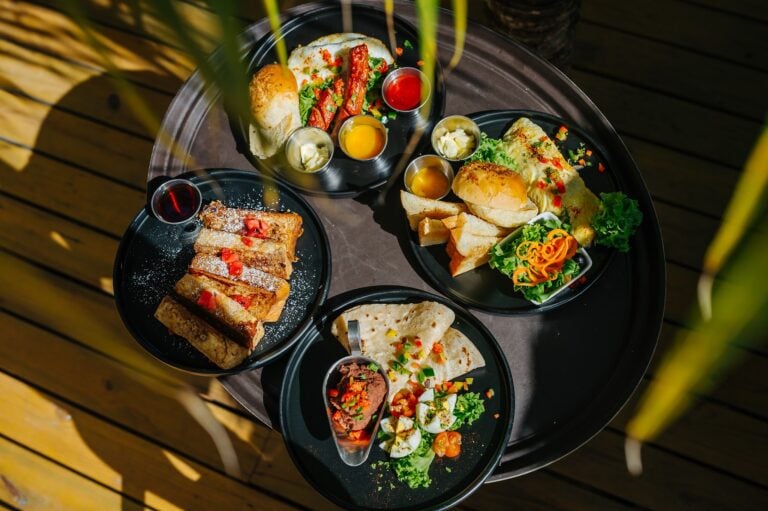 A variety of colorful Mexican dishes and desserts are served on black trays on a wooden table in Roatan, Honduras.