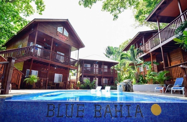 Three wooden holiday cottages in Roatan, Bay Islands, Honduras, surrounding a swimming pool with lounge chairs and lush tropical greenery.