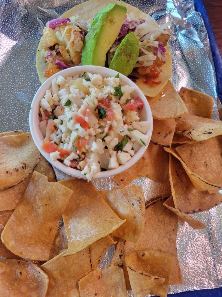 A plate of crispy tortilla chips served with a side of fresh ceviche containing chopped tomatoes, onions, and herbs, accompanied by two slices of avocado in a business setting in Roatan, Honduras.