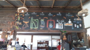 A brightly colored chalkboard menu showcasing food and drink options is displayed inside a restaurant in Roatan, Honduras, with wooden beams and decorative driftwood accents on the ceiling.