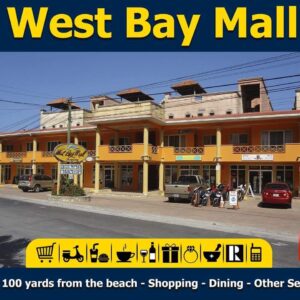 A colorful commercial building with a yellow and orange facade houses shops and businesses at West Bay Mall in Roatan, Honduras, with parked cars, motorcycles, and signage indicating shopping, dining, and services nearby.