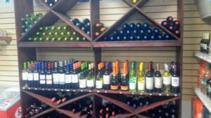 A wooden wine rack display in a store on Roatan, Honduras, holding various bottles of wine with colorful caps and neatly organized around different sections.