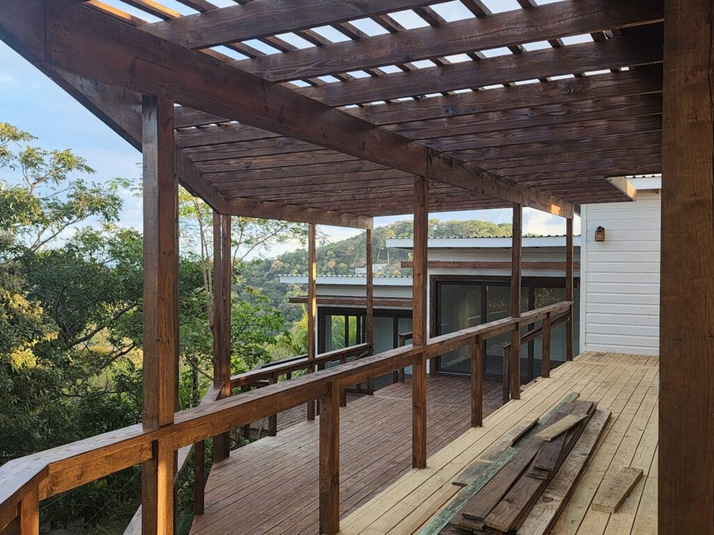 A partially constructed wooden balcony or deck with railings overlooking lush green trees and hills in Roatan, Honduras.