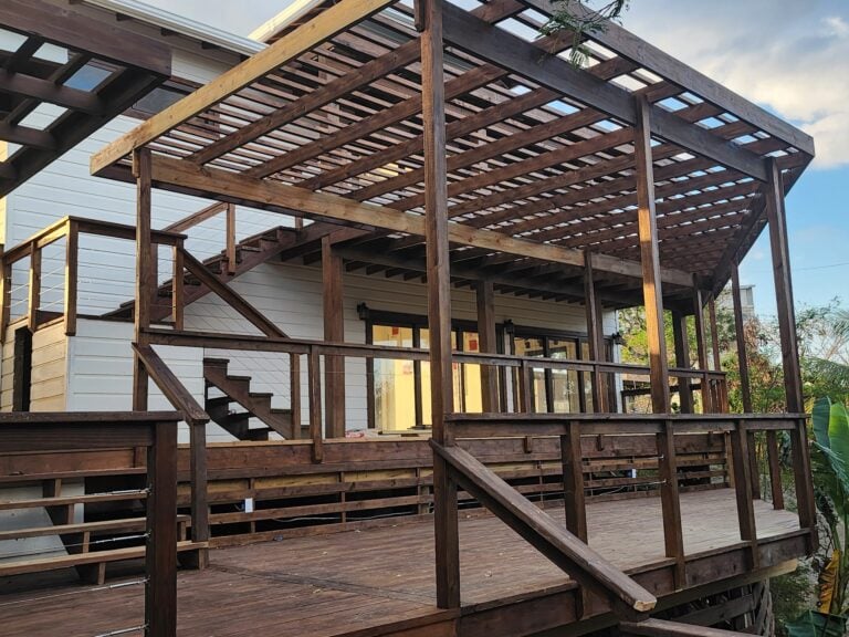 A multi-level wooden deck with stairs and railing is attached to a white building in Roatan, Honduras, with a partly cloudy sky in the background.