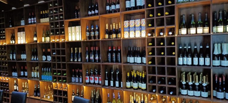 A wooden wine rack display in a business on Roatan, Honduras, showcasing various bottles of wine and champagne arranged in labeled sections.