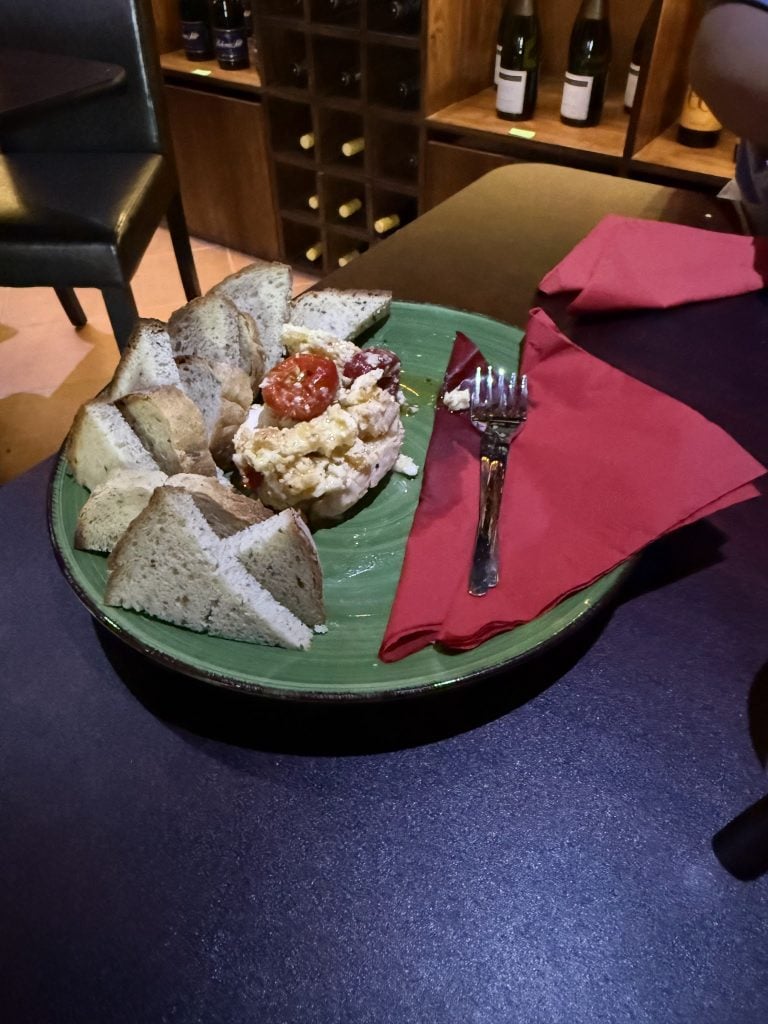 A green plate of bread, cheese, and sliced tomatoes is placed on a black table with a pink napkin, in a restaurant setting in Roatan, Honduras.