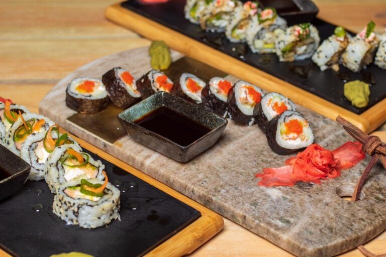 A variety of colorful sushi rolls with wasabi, ginger, and soy sauce served on wooden and stone trays showcase the culinary offerings in Roatan, Honduras.